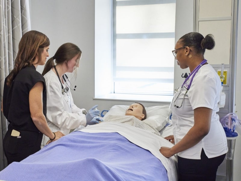 Two students and faculty observing a simulation manikin